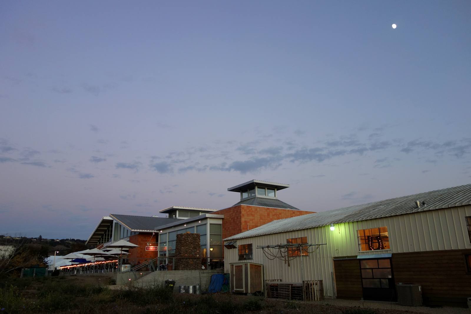 The riverfront side of Oxbow Public Market at dusk, seen from the Oxbow Commons side of the Napa River bend. The Commons, the park between the market and the river trail, hosted Saturday’s Trick or Vote rally.