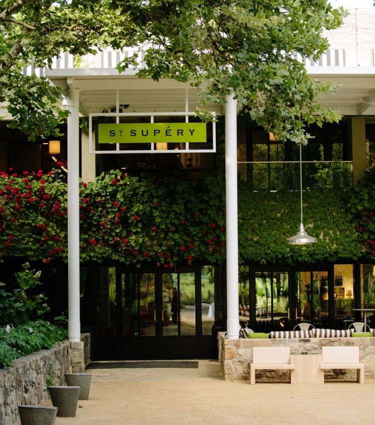 The signed entrance of St. Supery Estate Vineyard & Winery's Rutherford tasting room, framed by roses and live oaks.