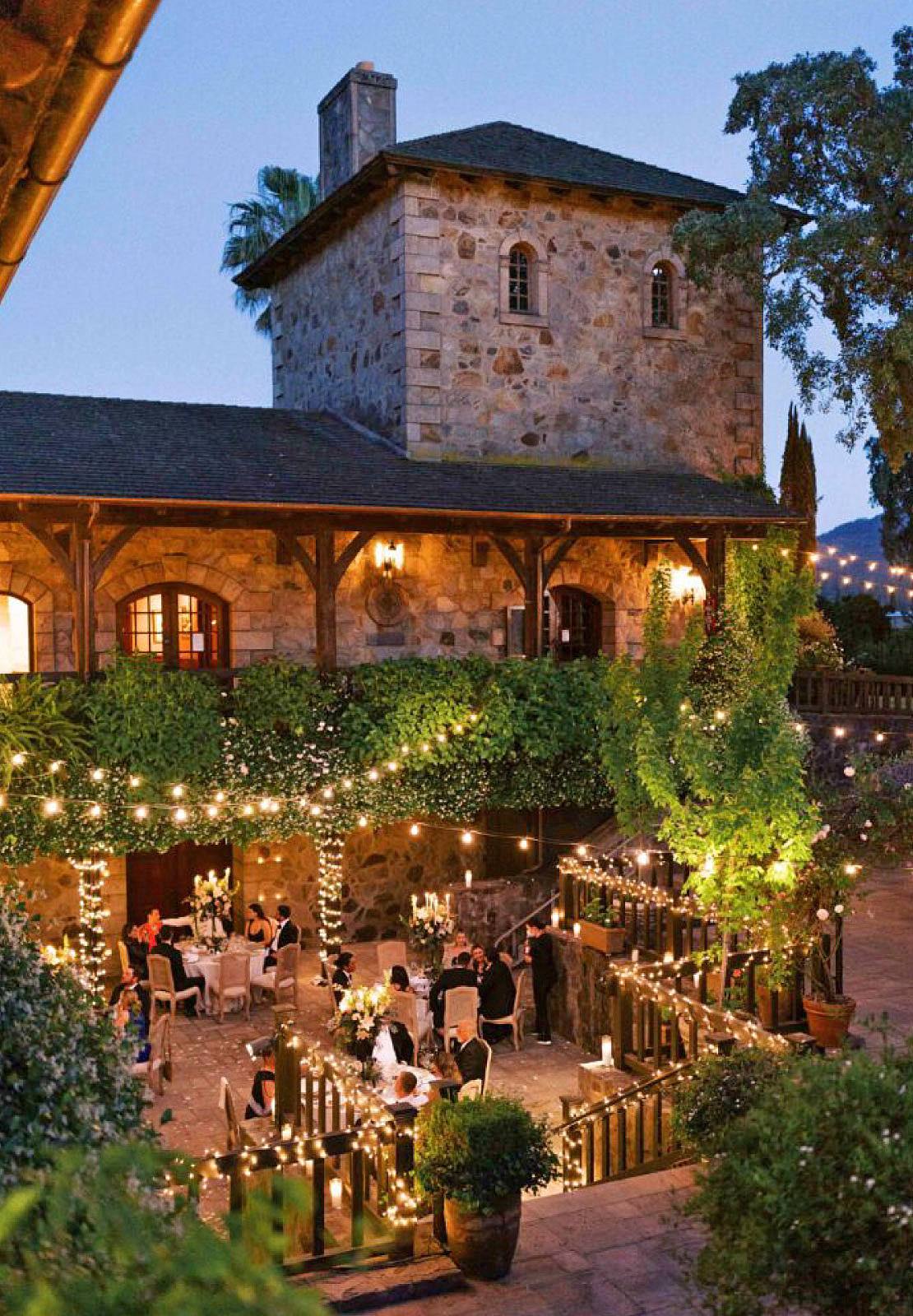 The stone tower of V. Sattui Winery lit up at dusk, guests dining on the terrace below.